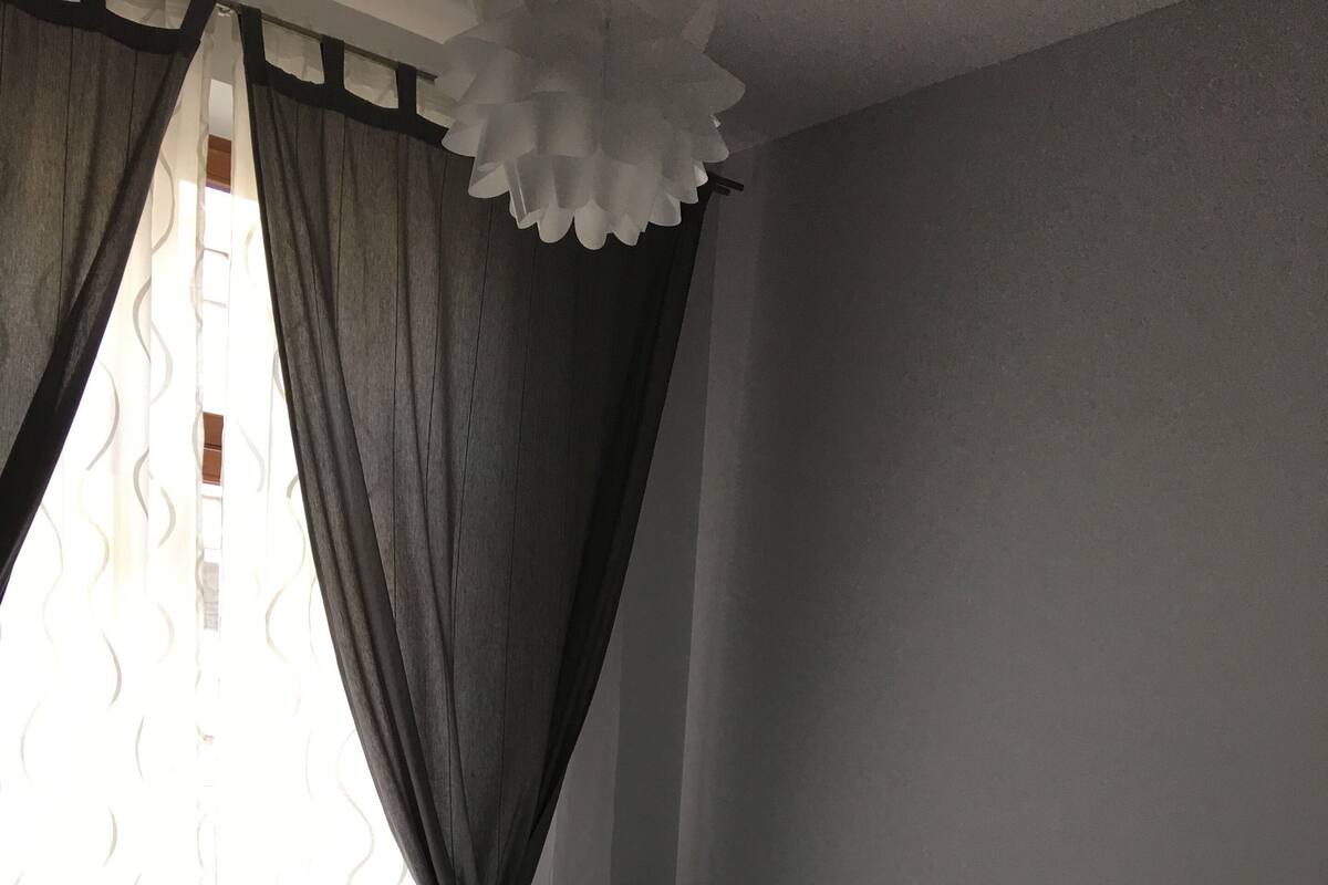 Quarto com cama, roupa de cama branca, cabeceira e janela com cortinas.