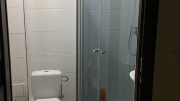 Un baño con inodoro, ducha con mampara de vidrio y pared de azulejos blancos.