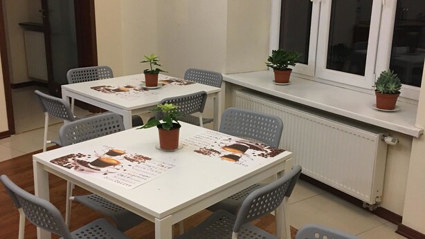 A small dining area with a white table and grey chairs, surrounded by potted plants. - Ametyst Hostel (Kraków)