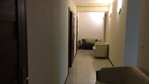 A hallway with a dark wooden door, a beige sofa, and a light-colored wall with a decorative ceiling pattern. - Ametyst Hostel (Kraków)