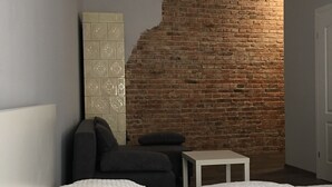 A room with two beds, a small table, a sofa, and a brick wall. - Ametyst Hostel (Kraków)