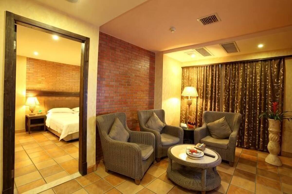 A hotel room with a bed, two armchairs, a small round table, a lamp, and a curtain with a golden pattern.