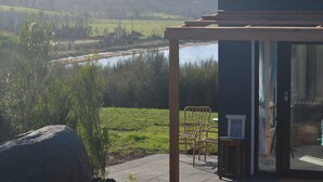 A covered outdoor seating area with chairs and a table, overlooking a river and green fields. - Flotsam Studio Accommodation (Dunalley)