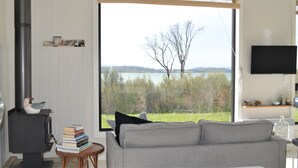 A living room with a large window, a fireplace, a sofa, and a television. - Flotsam Studio Accommodation (Dunalley)
