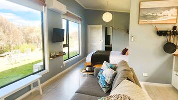 A modern bedroom with a large window, a flat-screen TV, and a bed with a headboard.