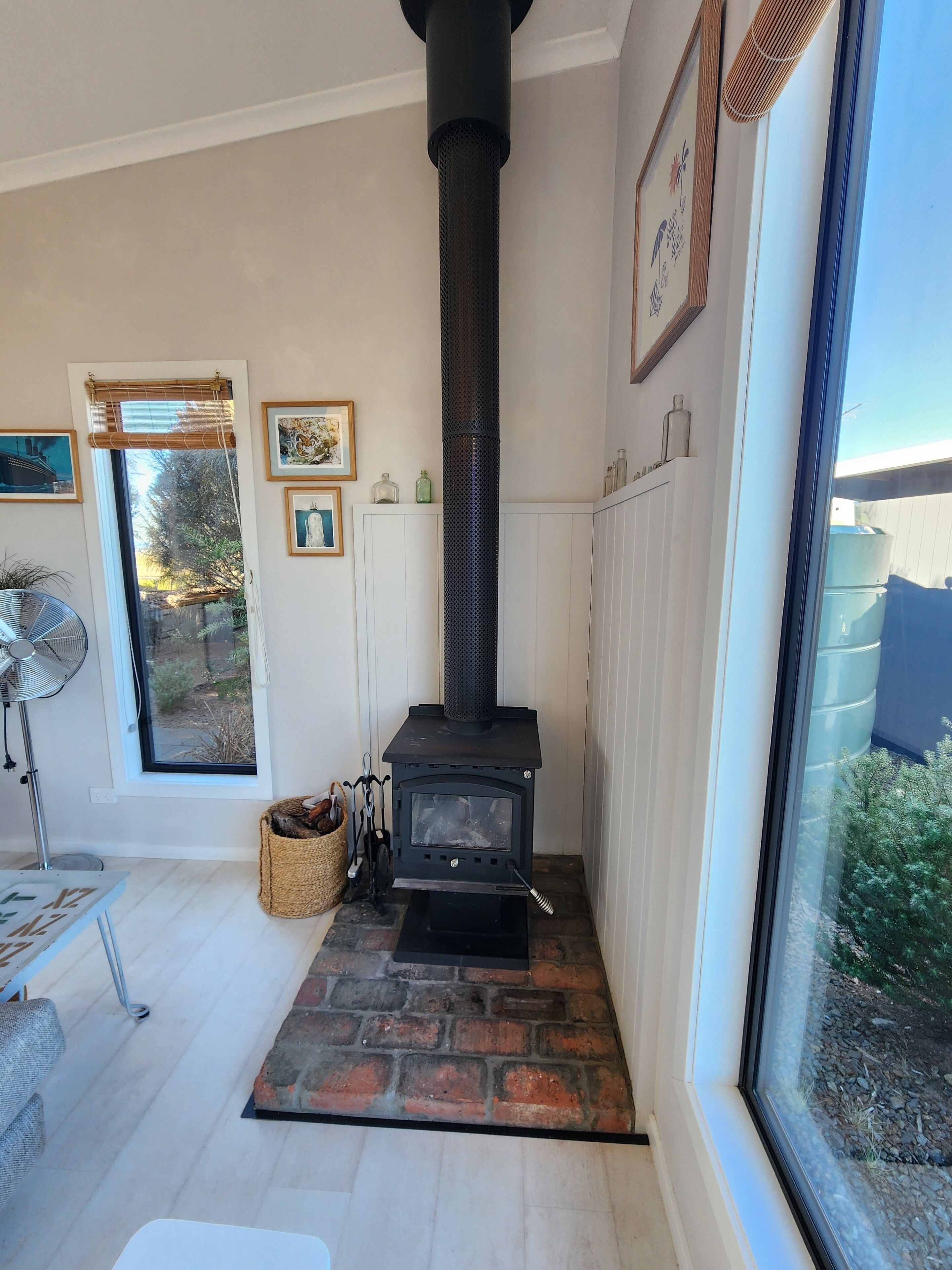 A room with a black wood-burning stove, a large window, and a fan.