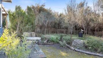 Un pati amb taula i cadires, envoltat de vegetació arbustiva i arbres.