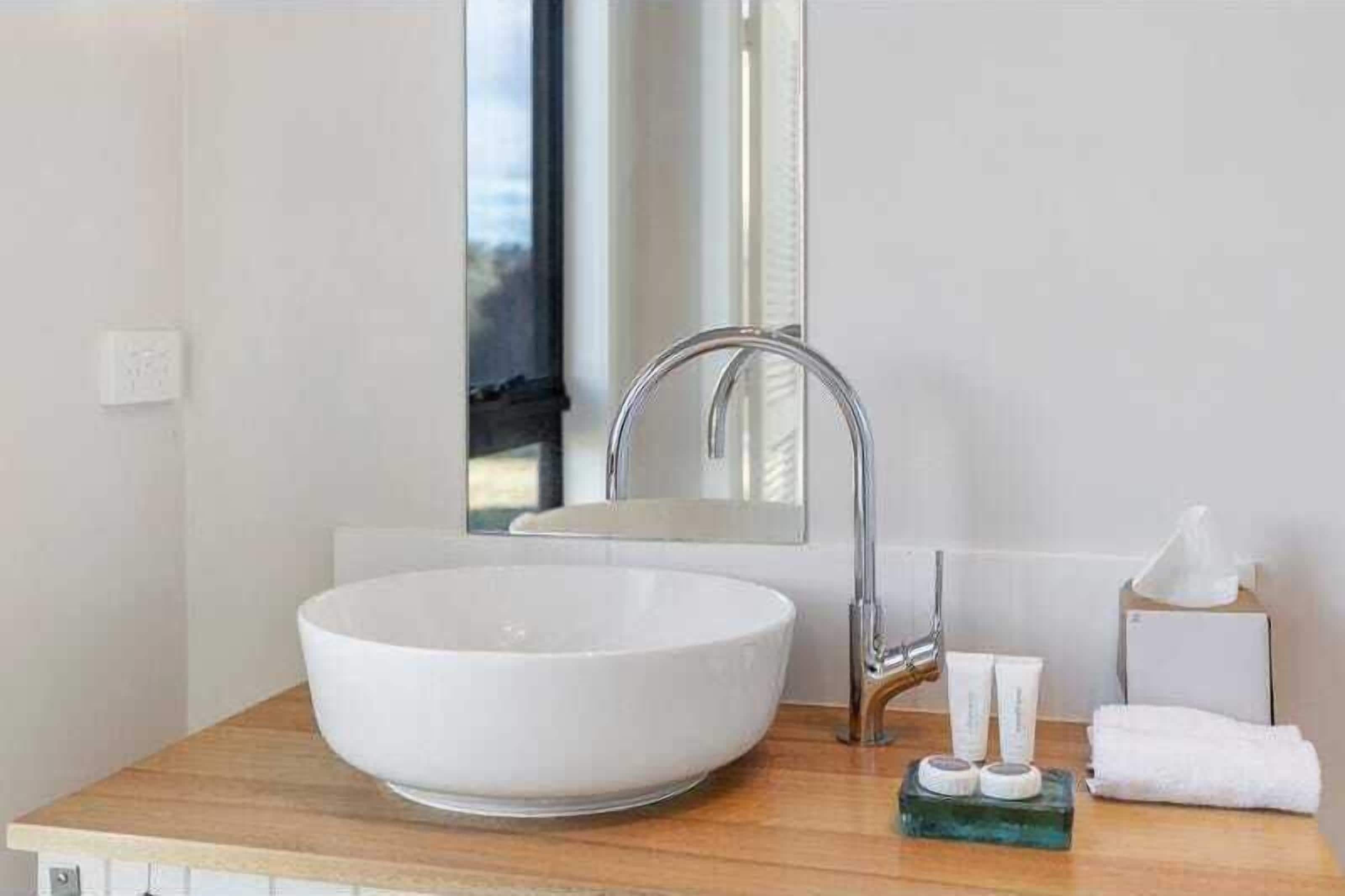 Un baño moderno con un lavabo blanco de diseño, un grifo cromado, un espejo y artículos de tocador sobre la encimera.