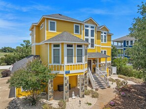 A two-story yellow house with a front porch, stone pillars, and a small garden with a Buddha statue.