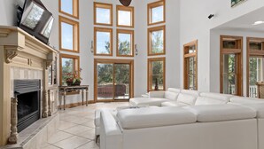 Ein geräumiges Wohnzimmer mit Kamin, großen Fenstern und einem weißen Ledersofa.