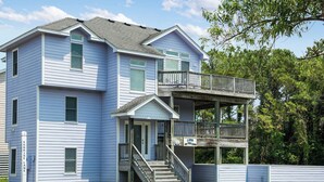 A two-story building with a balcony on the second floor, a front entrance with a staircase, and a sign that reads "LION ONE THE GARDEN". - Lion On The Sand: Oceanside 6-bedroom, Private Pool & Hot Tub (Corolla)