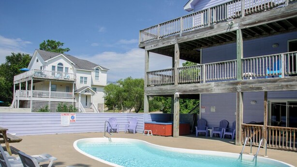 A two-story building with a pool area, including a pool, lounge chairs, and a wooden deck. - Lion On The Sand: Oceanside 6-bedroom, Private Pool & Hot Tub (Corolla)