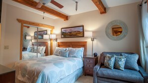 A bedroom with a bed, a nightstand, a chair, a ceiling fan, a painting, and a mirror. - Ten Mile Suites 103, Breckenridge (Breckenridge)