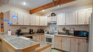 A kitchen with white cabinets, a granite countertop, a stove, a microwave, and a coffee maker. - Ten Mile Suites 103, Breckenridge (Breckenridge)