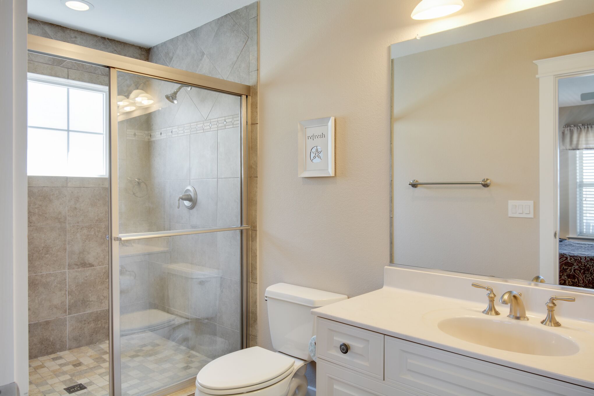 A bathroom with a glass-enclosed shower, a white toilet, and a large mirror above a sink with two faucets.
