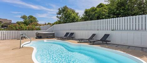 Una piscina amb un solàrium blanc, un banyera d'hidromassatge i gandules.
