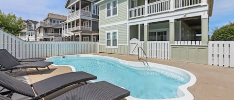 A swimming pool with lounge chairs and a wooden deck, surrounded by a white picket fence.