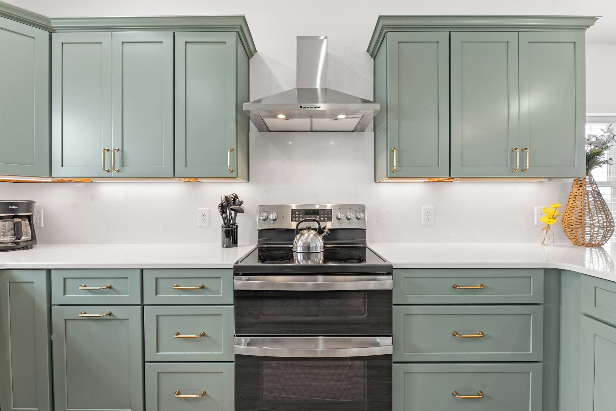 A kitchen with teal cabinets, stainless steel appliances, and a kettle on the stove.