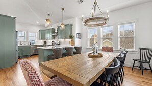 Une cuisine moderne avec un îlot central en bois, des luminaires suspendus et un coin repas comprenant une banquette et des chaises.