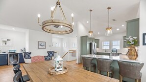 Un vaste espace dédié à la salle à manger, avec une table en bois, des chaises à revêtement gris et des luminaires suspendus.