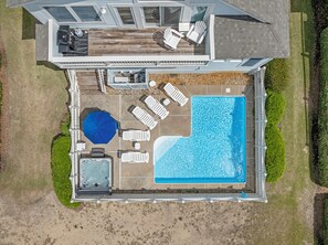 An aerial view of a house with a swimming pool, deck chairs, and a hot tub.