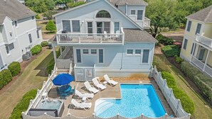 Une maison à deux étages avec une piscine dans le jardin, un jacuzzi et un patio couvert équipé de chaises longues.
