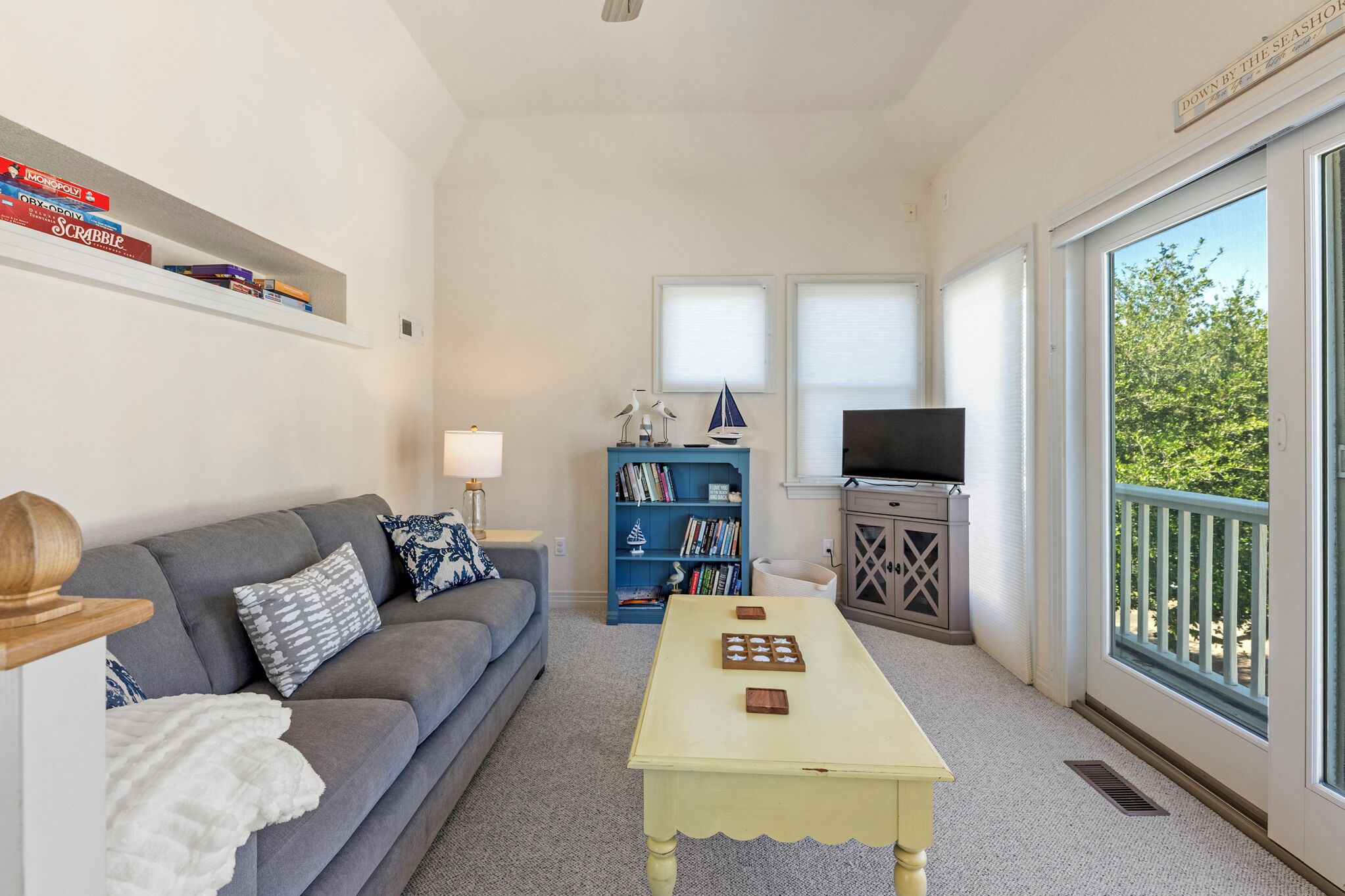 A living room with a sofa, a coffee table, a bookshelf, a television, and a balcony with a view.