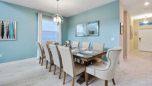A dining room with a rectangular table, six chairs, a chandelier, and a large mirror on the wall.
