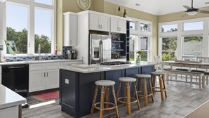 A modern kitchen with a large island, white cabinets, and a dining area with a table and chairs. - Y7 Fairways & Sunsets: Pool, Spa, Elevator (Corolla)