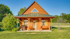 A wooden cabin with a triangular roof, a porch with seating, and a grill area. - Lakefront Vacation Rental w/ Patio & Grill! (Columbia)