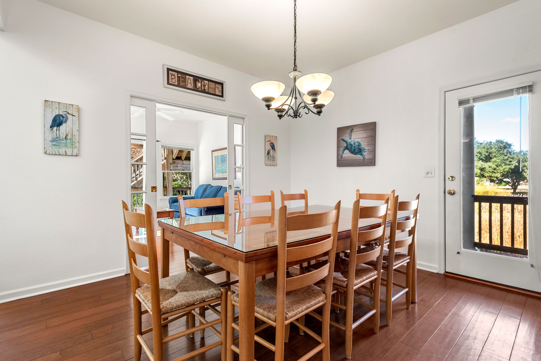 A dining area with a glass-top table and wooden chairs, a chandelier, and artwork on the walls.