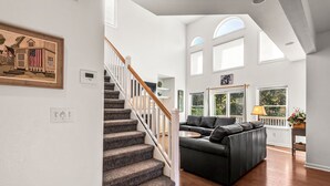 Ein geräumiger Wohnbereich mit Treppe, einer schwarzen Ledersofa und einem großen Fenster, das natürliches Licht hereinlässt.