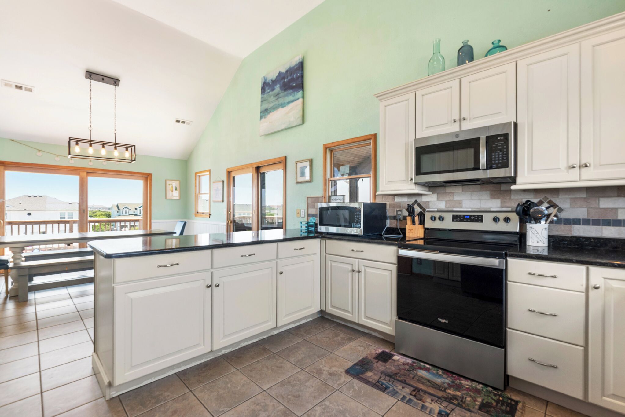 A spacious kitchen with white cabinets, a large island, stainless steel appliances, and a view of the mountains through large windows.