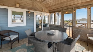 Un espace extérieur aménagé, abrité et doté d'une table ronde et de chaises en osier, d'un plafond en bois et de grandes fenêtres offrant une vue sur les environs.