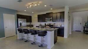 Una cocina moderna con armarios de madera oscura, electrodomésticos de acero inoxidable, una isla central con taburetes y luces empotradas en el techo.