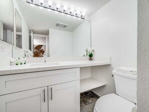A bathroom with a white vanity, a large mirror with lights, a toilet, and a shower area. - Roomy Suite w/Modern Open Kitchen, Washer/Dryer, WiFi, Lanai–Kamaole Sands 3301 (KIHEI)