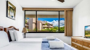 Une chambre d’hôtel équipée d’un lit, d’une télévision, d’une commode et d’une fenêtre donnant sur des bâtiments et des espaces verts.