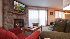 Una sala de estar acogedora con chimenea de piedra, un televisor montado en la pared, un sofá cómodo y una mesa de centro de madera.