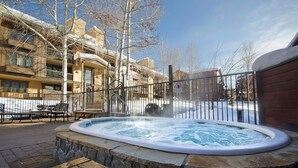 A hot tub surrounded by a stone wall, with a metal fence and benches nearby.