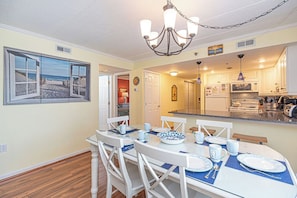 A dining area with a table set for four, a chandelier, and a kitchen in the background.