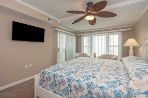 A hotel room with a bed, a ceiling fan, a TV, a chair, and a window with curtains.