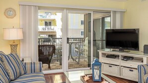 Un salón con sofá, televisión y un balcón con mobiliario exterior.