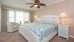 Un dormitorio con una cama, dos mesitas de noche, una silla, un ventilador de techo y una ventana con persianas.