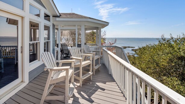 Une terrasse en bois avec des rampes blanches, un espace salon couvert avec des chaises et une vue sur la mer.