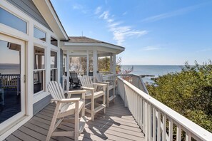 A wooden deck with white railings, a covered seating area with chairs, and a view of the sea.