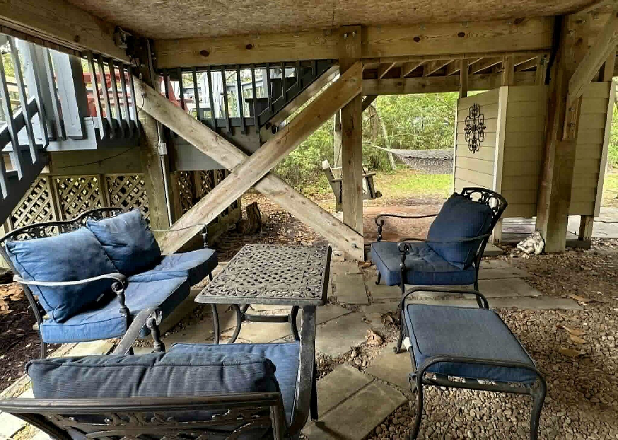 A covered outdoor seating area with a table and two chairs, a staircase, and a decorative wall.