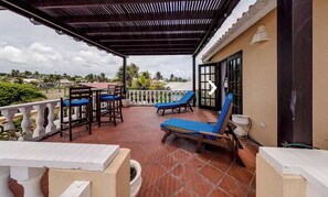 Relax in this serene outdoor space with a wooden pergola overhead, surrounded by palm trees and a distant view.