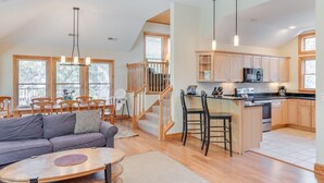 A spacious living area with a sofa, dining table, and chairs, a kitchen with wooden cabinets and appliances, and a staircase leading to an upper level. - Sound Dreams: Private Pool, Spa (Corolla)