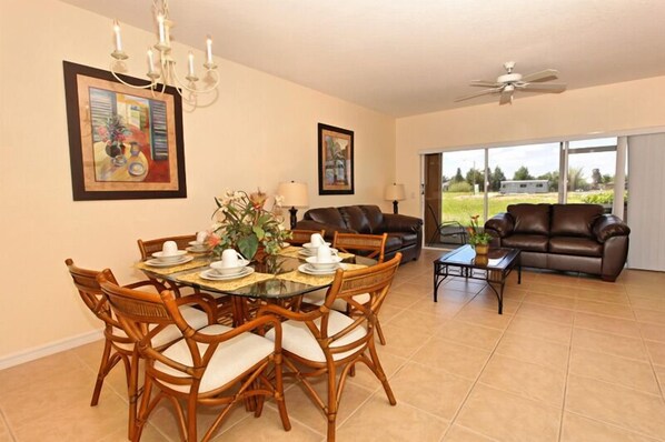 A dining area with a round table, chairs, and a chandelier. There is a sofa and a coffee table in the background. - ⛱ Legacy Park -2 Bed Town Home - Communal Pool ✈ (Davenport)
