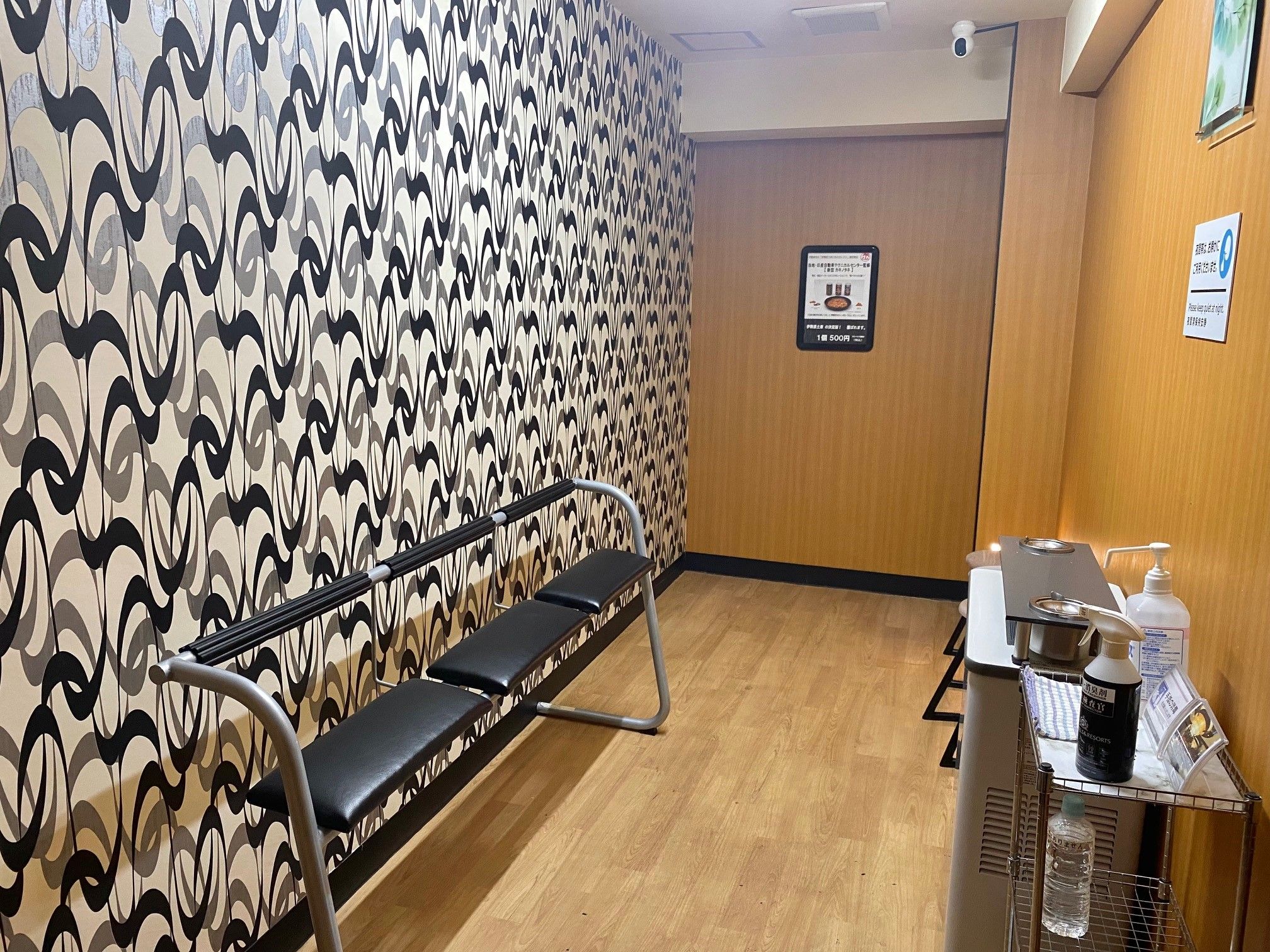 Une salle d'attente avec un mur décoré, un banc, un comptoir d'accueil équipé de quelques commodités et un panneau affiché sur le mur.